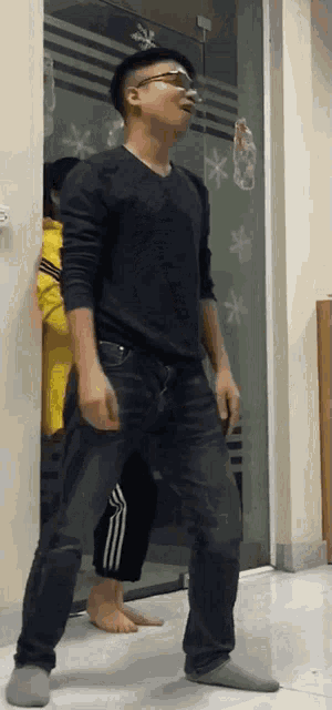 a man in a black shirt and jeans is standing in a doorway .