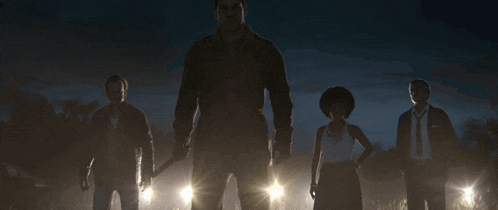a group of people standing in a dark field with a man holding a knife