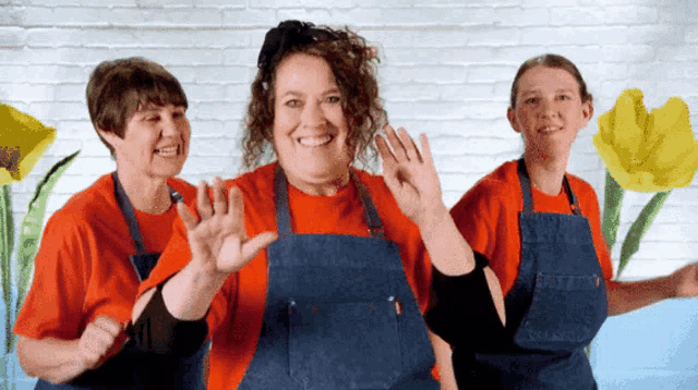 three women wearing red shirts and blue aprons are dancing