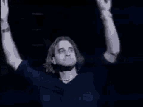 a man in a blue shirt is raising his arm in the air .