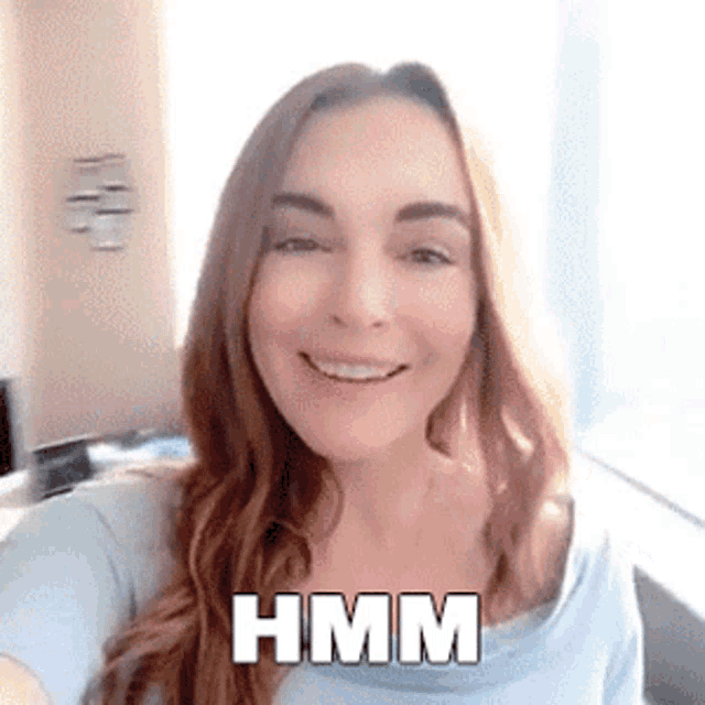 a woman in a blue shirt is smiling and has the word hmm written on her face .