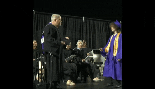 a man in a graduation cap and gown is shaking hands with a woman in a purple gown .