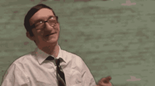 a man with glasses and a tie gives a thumbs up