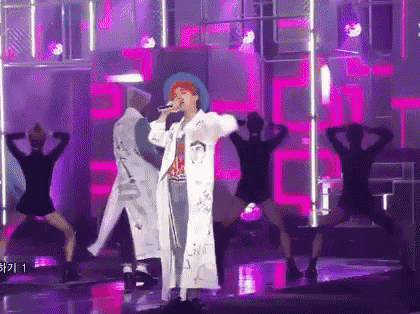 a man is singing into a microphone on a stage while a group of dancers are dancing in the background .
