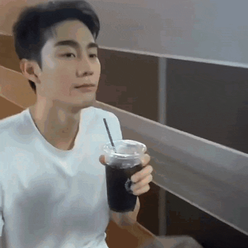 a man in a white shirt is holding a cup of iced coffee with a straw .