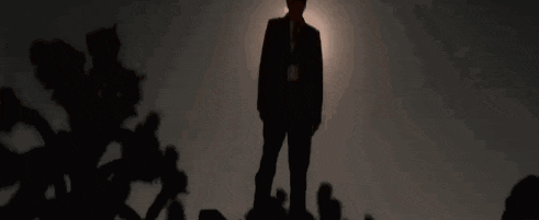 a man in a suit and tie is standing in front of a sunset .