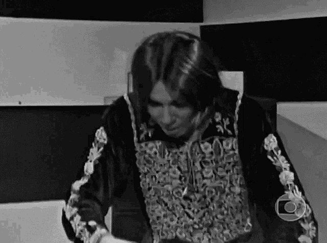 a black and white photo of a man with long hair wearing a black jacket with embroidered sleeves .
