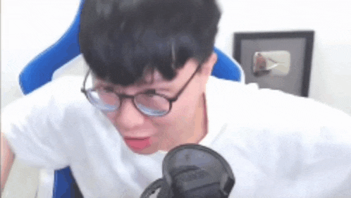 a man wearing glasses and a white shirt is sitting in a chair in front of a microphone .