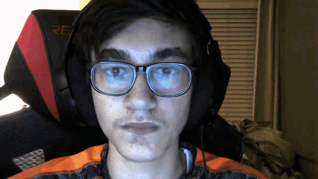 a man wearing glasses and headphones sits in a chair that says re on it