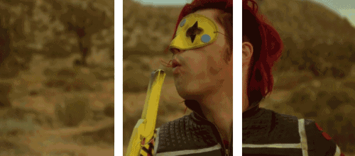 a man with red hair and a yellow mask on his face blowing a balloon
