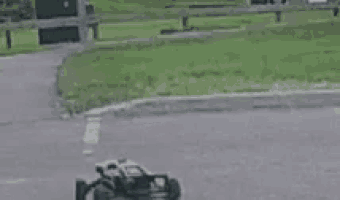 a remote control car is driving down a road next to a grassy field .