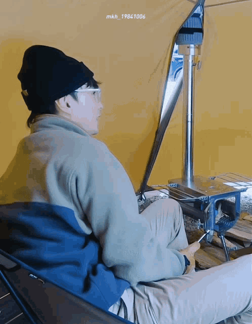 a man wearing a beanie and glasses is sitting in front of a tent with the year 1984 written on the bottom