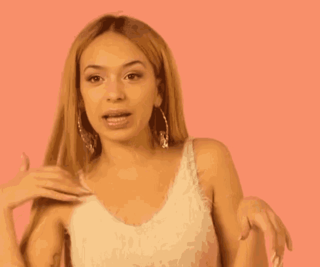 a woman in a white tank top and hoop earrings is making a funny face with her mouth open .