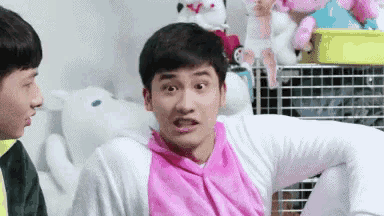 a man in a pink shirt is making a funny face while sitting next to another man in a white shirt .