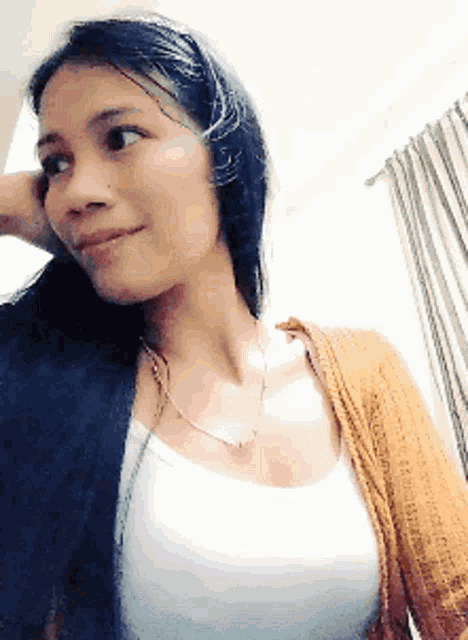 a woman wearing a white tank top and an orange sweater is smiling