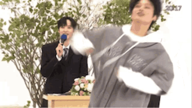 a man in a suit and tie is holding a microphone while a man in a hoodie is dancing .