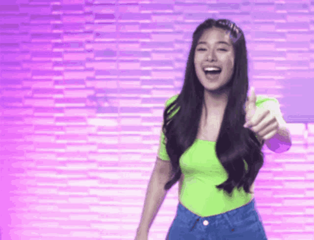 a woman in a neon green shirt and blue jeans is giving a thumbs up sign .