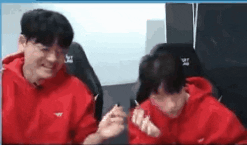 two men in red hoodies are sitting next to each other in a room and laughing .