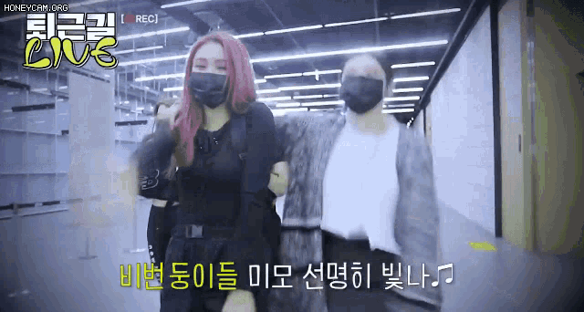 two women wearing face masks are standing next to each other in a hallway .