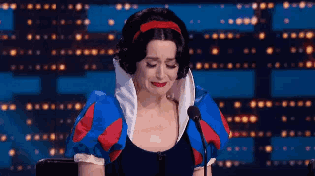 a woman in a snow white costume is crying while speaking into a microphone
