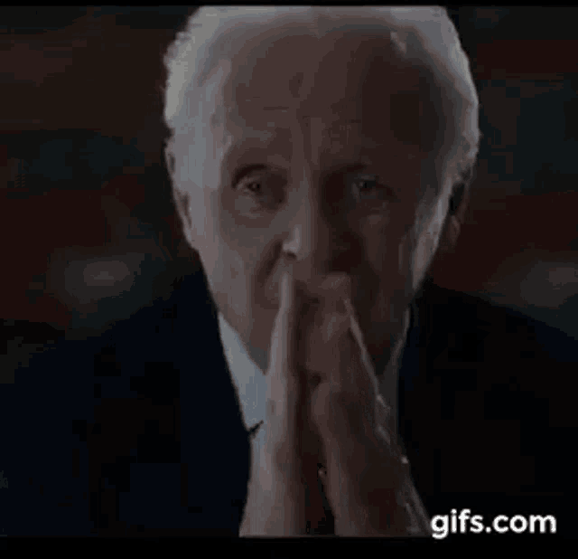 a man in a suit and tie is praying with his hands folded in front of his face .