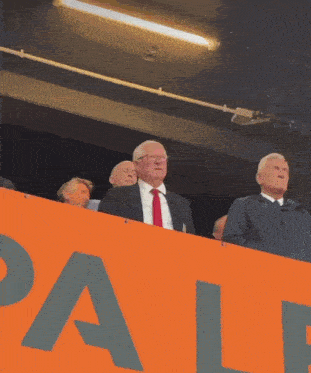 a man in a suit and tie stands in front of a large orange sign that says pale
