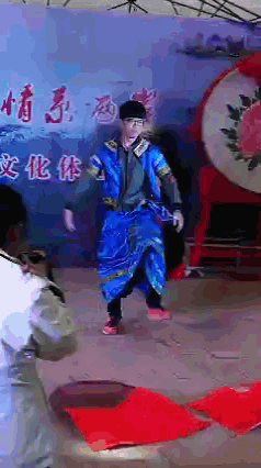 a man in a blue dress is dancing in front of a wall with chinese writing