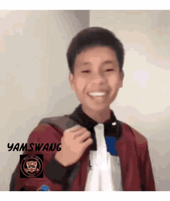 a young boy wearing a red jacket and a white shirt is smiling and holding a backpack .