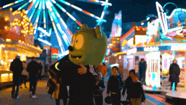 a man in a gummy bear costume stands in front of a ferris wheel at an amusement park
