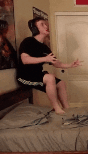 a man wearing headphones is sitting on a bed holding a remote control