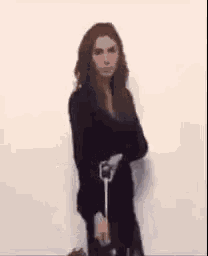 a woman is standing in front of a white wall holding a vacuum cleaner in her hand .