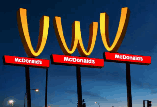 three mcdonald 's signs are lit up at night with a blue sky in the background
