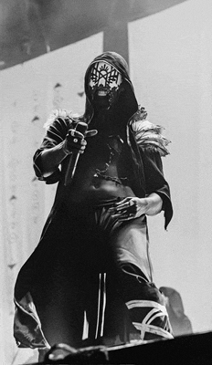 a black and white photo of a man wearing a mask and a hood holding a microphone