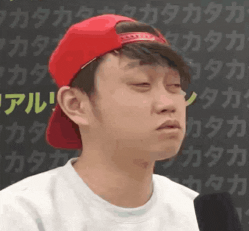 a young man wearing a red hat and a white shirt is making a funny face with his eyes closed .