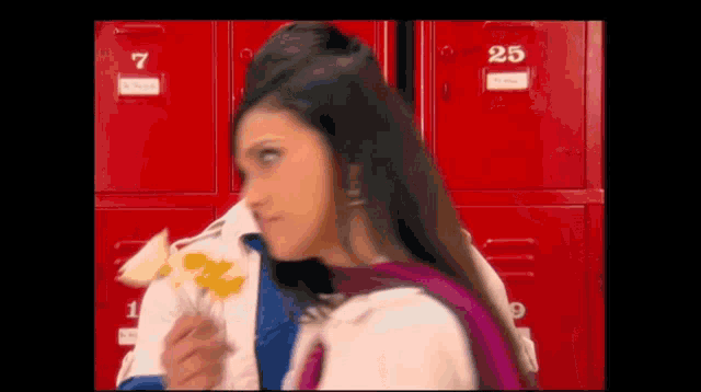 a girl is standing in front of a row of red lockers and eating chips .