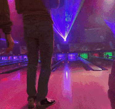 a person standing in a bowling alley with purple lights behind them