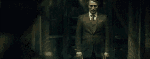a man in a suit and tie is standing in a dark hallway holding a knife .