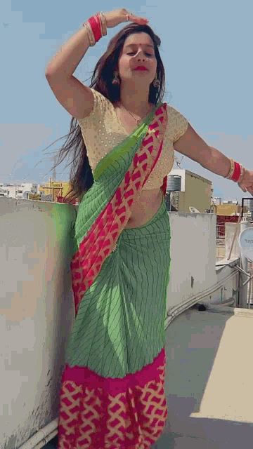a woman in a green and pink saree stands on a rooftop