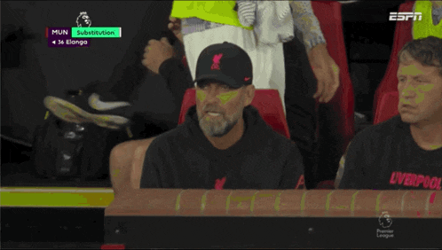 a man wearing a liverpool hat sits in the stands watching a soccer game