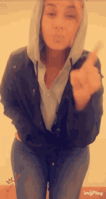 a woman wearing a hooded jacket and jeans giving the middle finger