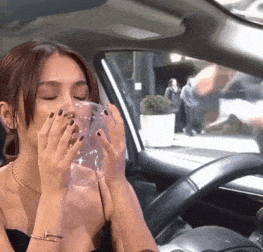 a woman in a car is blowing a bubble out of a clear cup
