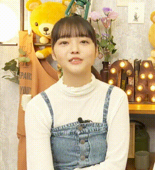 a woman in a white shirt and blue overalls is sitting in front of a yellow teddy bear and flowers .