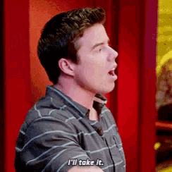 a man in a striped shirt is standing in front of a red wall and says i 'll take it .