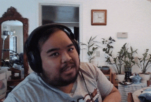 a man wearing headphones in a living room with a clock on the wall behind him