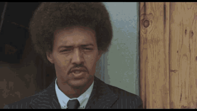 a man in a suit and tie is standing in front of a wooden door with his eyes closed
