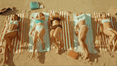 a group of women laying on striped towels on a beach