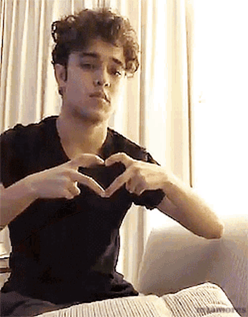 a young man in a black shirt is making a heart shape with his hands