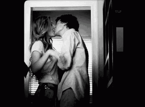 a man and a woman are kissing in front of a window with the letters tlp on the bottom right