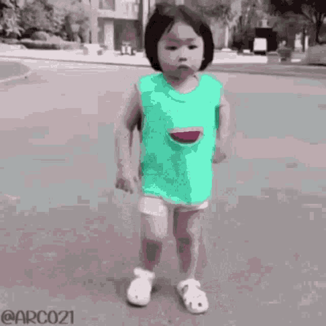 a little girl in a blue shirt and white shorts is dancing on the sidewalk .