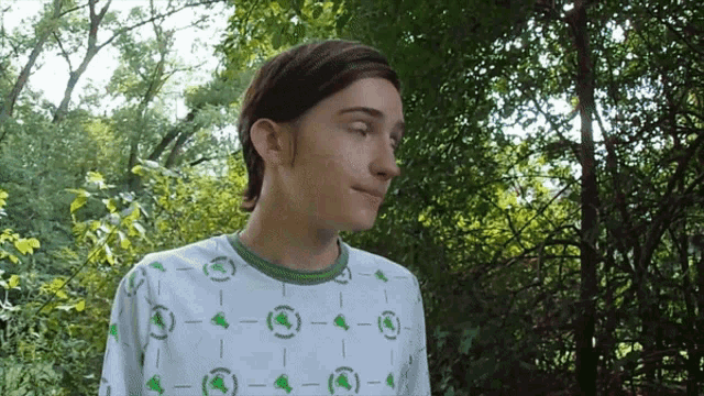 a woman wearing a white shirt with green circles on it stands in the woods